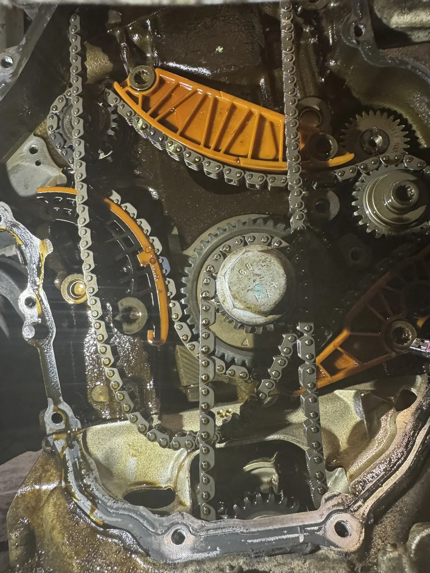 Car engine with timing chain, gears, and orange timing chain guides visible inside engine block.